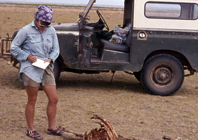 Gifford-Gonzalez in front of a safari truck writing in a notebook while looking at bones