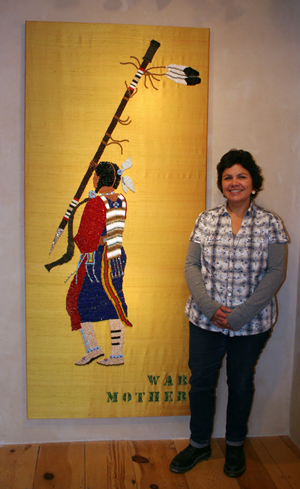 Greeves stands next to a six-foot beaded wall hanging she made that tells the story of cen