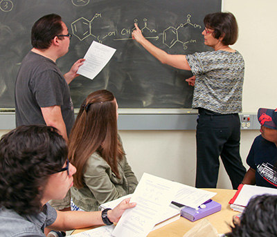 teacher explaining chemistry problem on blackboard