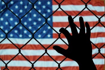 Photo of American flag with a silhouette of a hand on a chain-link fence