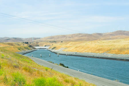 A public water delivery canal flowing through grass-covered hills in California