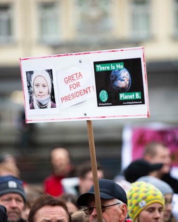 A man at a protest holds a sign with an image of Greta Thunberg 