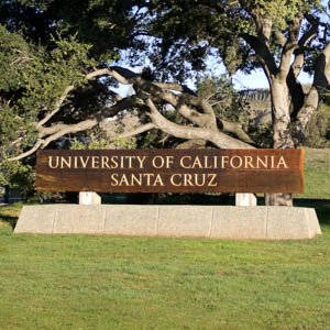 A sign shows the name University of California Santa Cruz in front of a tree on campus