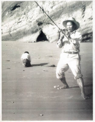 Man fishing on the beach with child in background