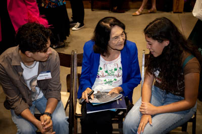 Dolores Huerta sits with two students and signs photos