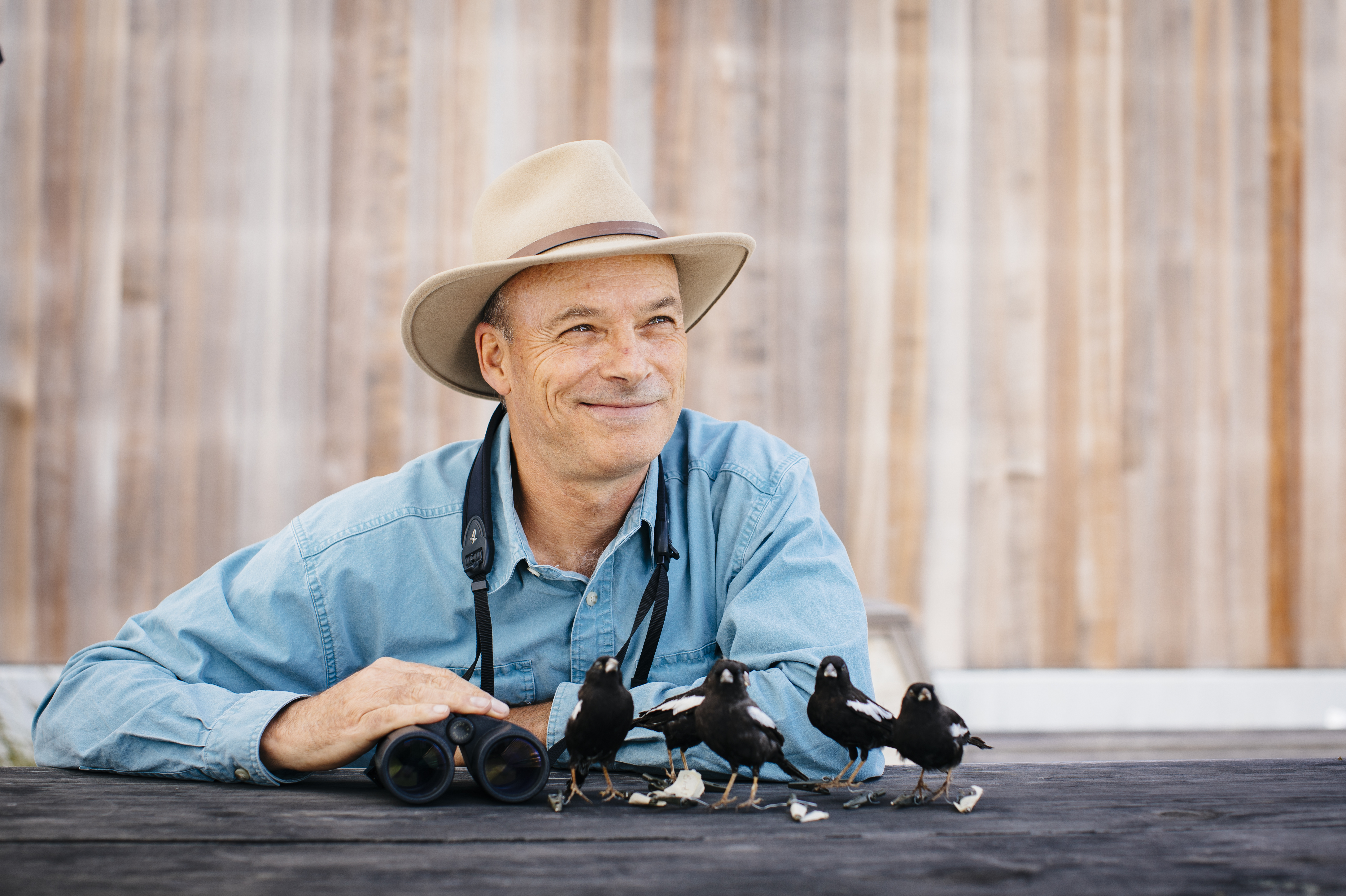 portrait of Bruce Lyon smiling away from the camera with figurines of little black birds