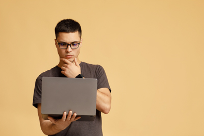 A young man with a puzzled expression holding a laptop computer