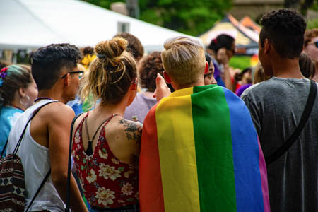 Young adults gathered outdoors at an event, some participants are wearing rainbow flags