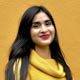 Roxanna Villalobos posing in front of a bright yellow wall