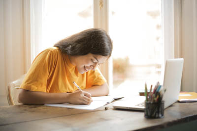 A student studies at home with a notebook and laptop