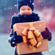 A child walking in the snow carrying a wrapped gift box