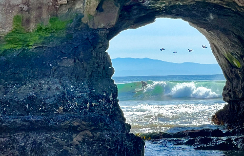 Picturesque view of Schulkin surfing, seen through a natural arch. Photo by John Sawyer