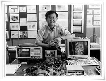 Black and white photo of Steve Kang leaning over old computers and a tangle of wires.