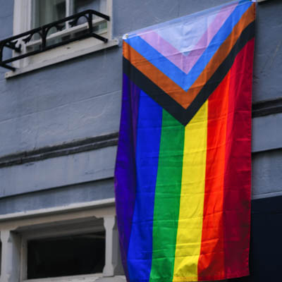 A progress pride flag is displayed on the exterior of a building