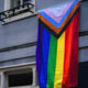 A progress pride flag is displayed on the exterior of a building