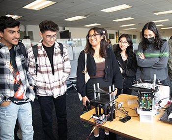 five students observe a lab-on-a-chip device.