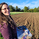 Colleen Josephson holds a microbial fuel cell in front of a plowed row of dirt.