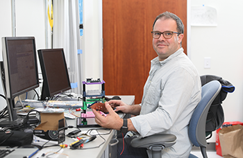 Prof Teodorescu sits at a computer with a chip in his hand.
