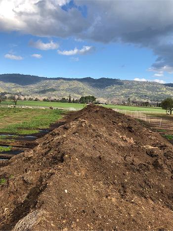 A pile of compost in a field with with mountains in the distance
