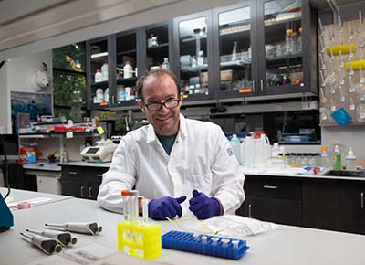 Ed Green in a lab coat, with test tubes and other lab equipment