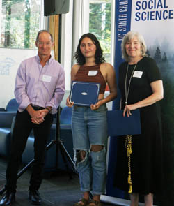 Photo of student with award plaque with faculty members