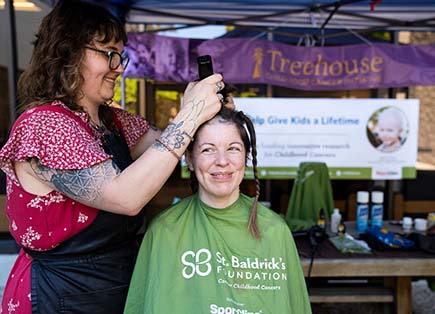 Two women smiling as one shave the hair off the other's head. 
