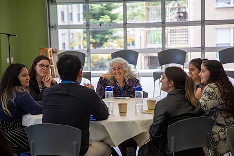 Group of students and faculty discuss around a table.