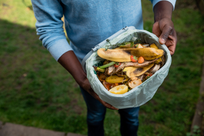 man's hands holding household compost collection bin with food scraps