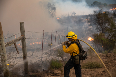 A firefighter sprays water on a fencepost in a rural area