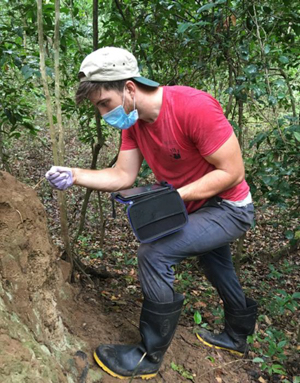 Seth Phillips in a forest in Africa poking a stick into a termite mound