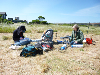 Students sit in a patch of dead dry grass with sensors taking notes