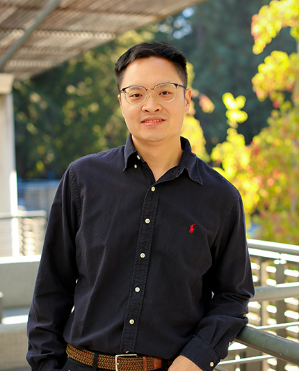 Portrait of Andy Yeh wearing a blue collared shirt with yellow trees in the background