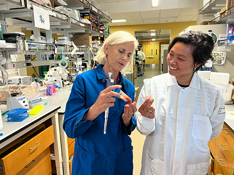 Forsberg and Poscablo, wearing lab coats and smiling, observe blood in a vial.