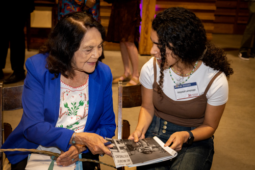 Dolores Huerta sitting with a young women holding an old photograph and talking