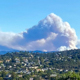 Wildfire smoke billowing behind a mountain ridge, with homes and forest in the foreground