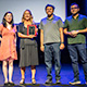 Getoor smiles on a stage holding an award plaque with three others