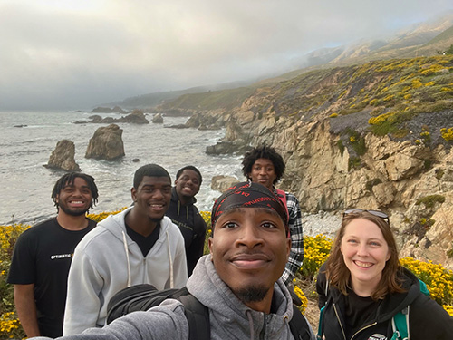 Six people take a selfie near cliffs above the ocean.