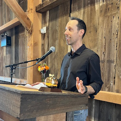 Jeffrey Erbig speaks at a podium with a metal golden apple