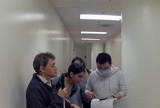 Three students gather around a phone, standing alongside a blind navigator.