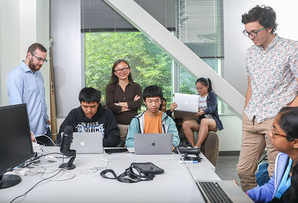 Sri Kurniawan stands behind a desk, where several students are working on computers