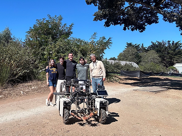 Five people stand smiling behind a robotic tractor on the UCSC farm