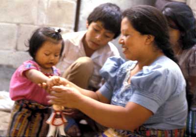 A woman and children work together to play with a wooden puppet toy