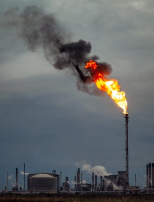 A flame on a tall stack in the foreground of oil refinery buildings