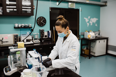 Vicky Oelze handles test tubes in a lab with many small machines