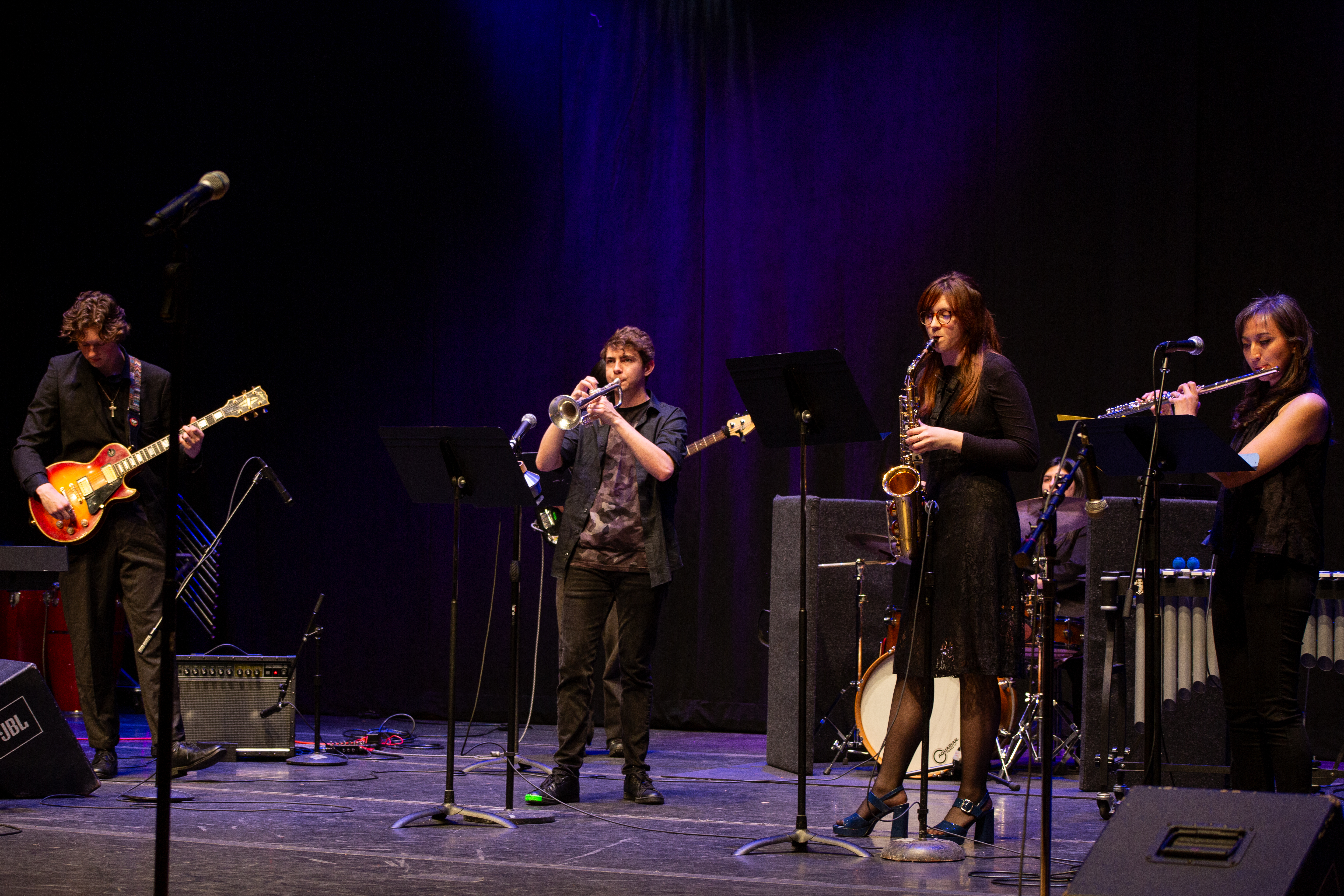Students on a stage play a guitar, trumpet, saxophone, and flute