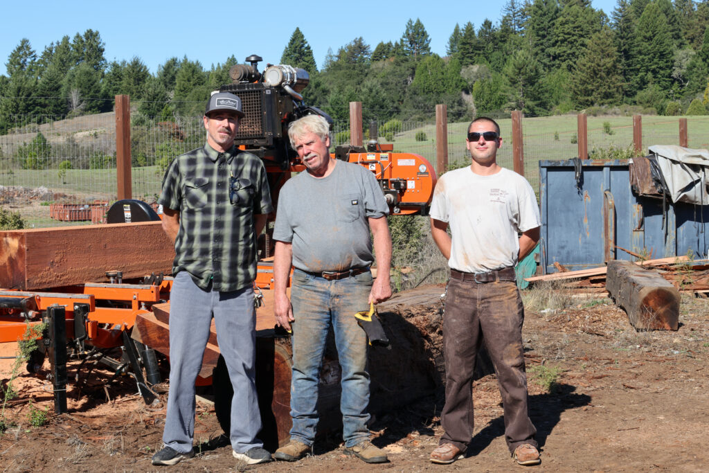 Three men standing in front of the portable sawmill.