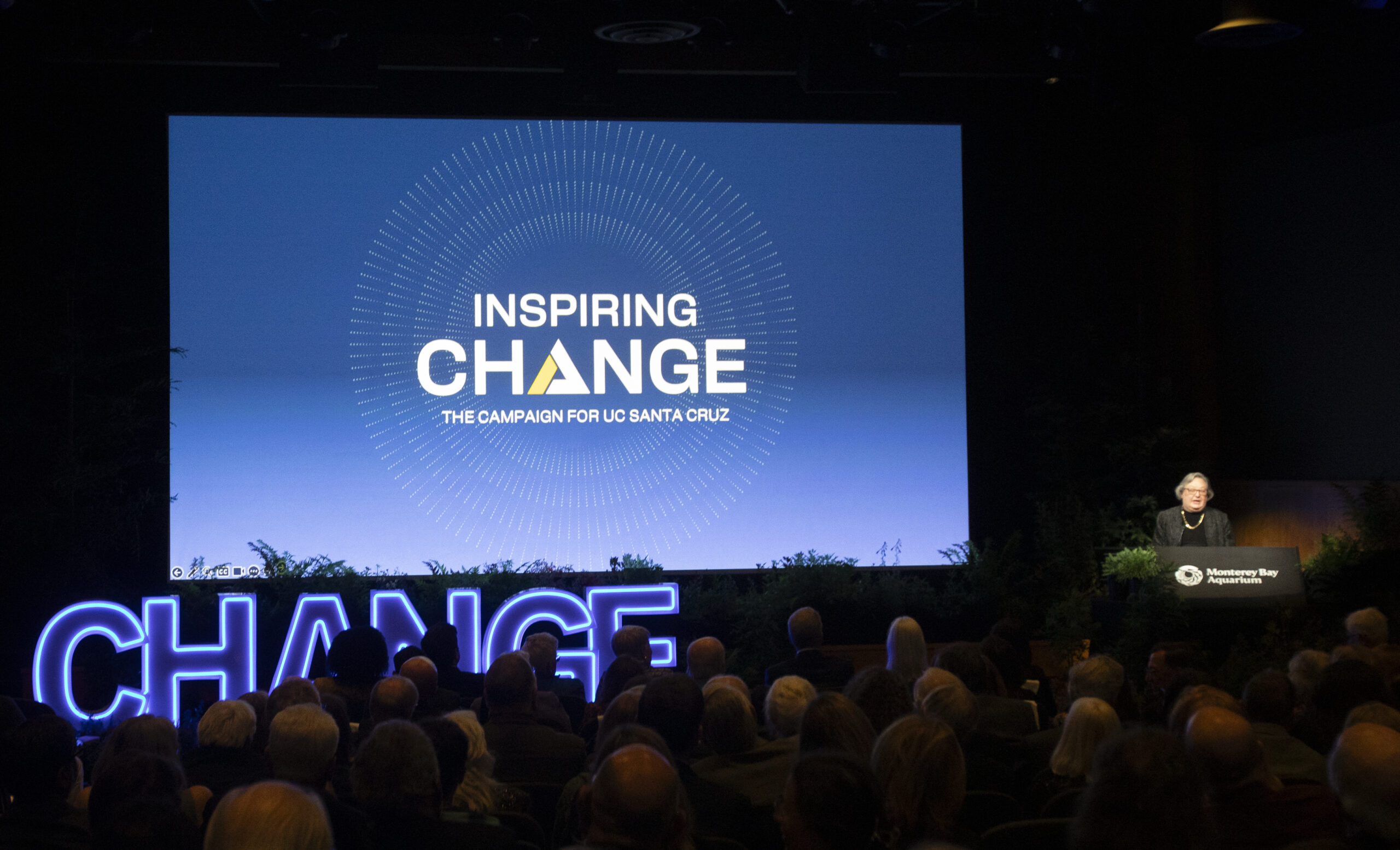 Chancellor Larive in an auditorium with the Inspiring Change logo projected on a screen.