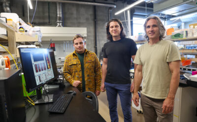 Three researchers smile at the camera in the lab.