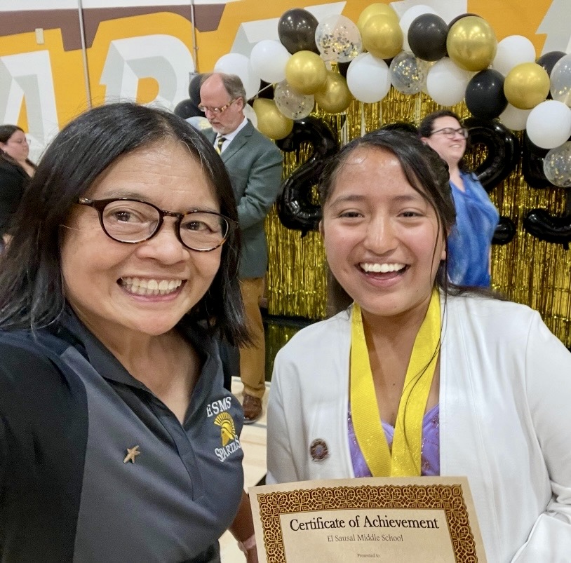 Smiling student at a celebration holding a certificate of achievement next to her teacher.
