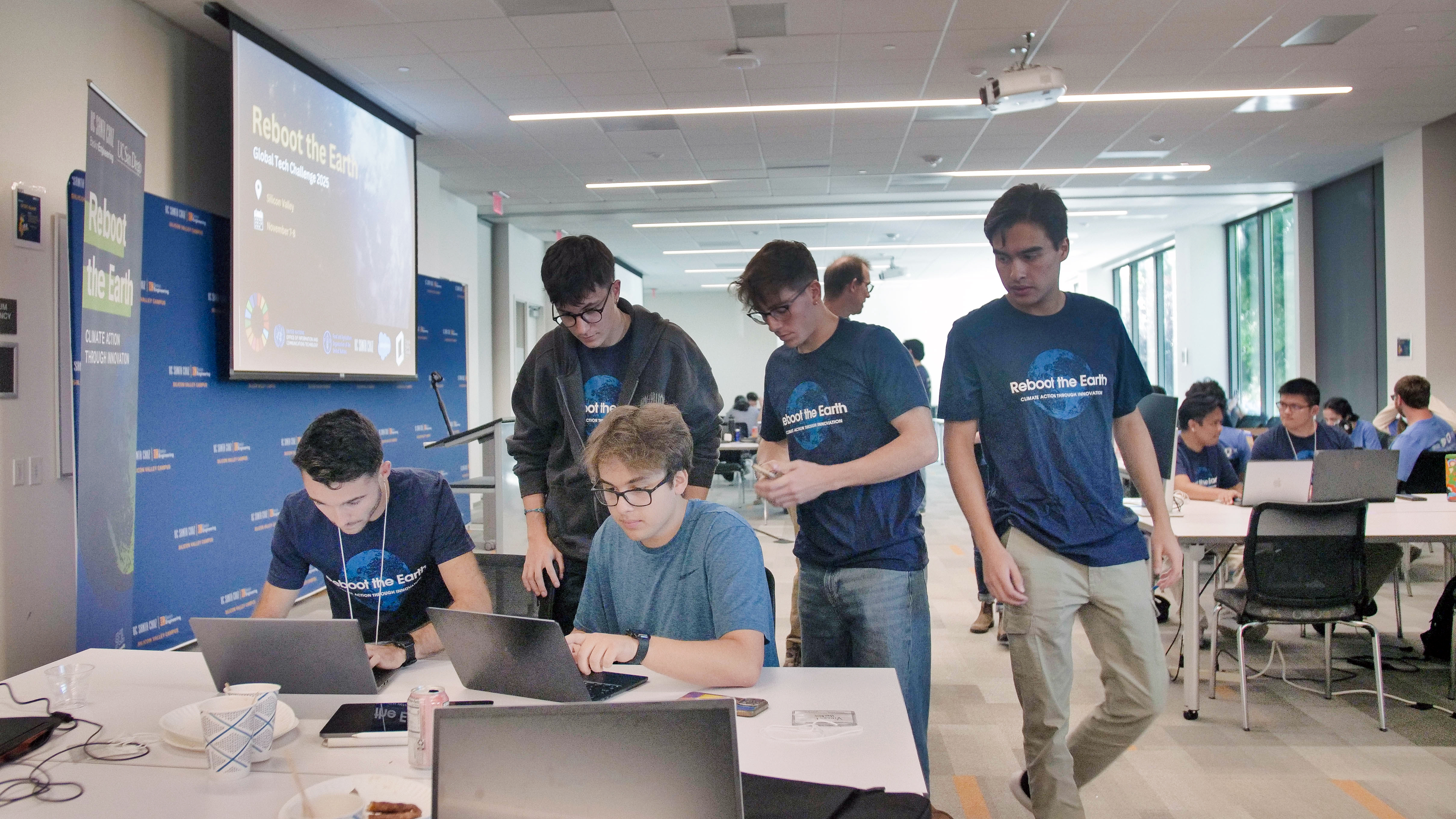 five students wearing 'reboot the earth' t-shirts collaborate around computers